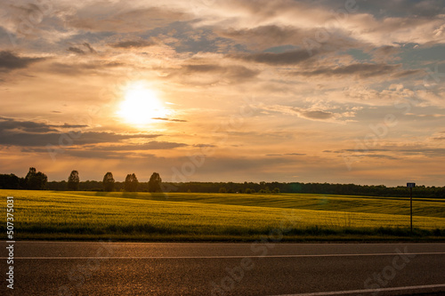 sunset, beautiful sky road in the warm rays of evening light and a large fiel...