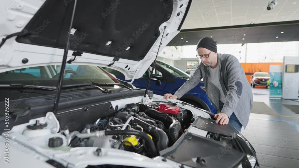 A man in a car showroom examines an engine under the hood. A man in a car showroom examines an engine under the hood.