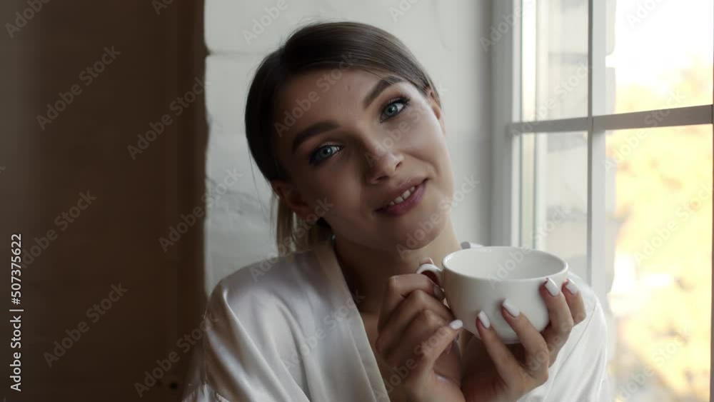 Attractive peaceful dreamy woman holding cup enjoy favourite tea drink morning invigorating coffee beverage while sit at desk in modern living room before start work. Break, pause, daydreaming concept Attractive peaceful dreamy woman holding cup enjoy favourite tea drink morning invigorating coffee beverage while sit at desk in modern living room before start work. Break, pause, daydreaming concept