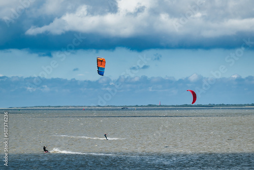 Two kitesurfers in stormy weather on the Wadden Sea in the north of the Netherlands, province of Groningen. On de horizon island and lighthouse of Ameland
 photo