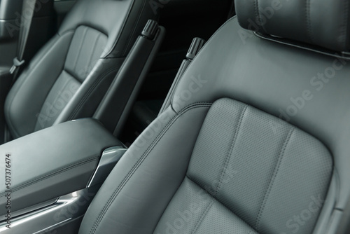 Close-up of a black genuine leather driver's seat with a folding armrest. Place for the logo. Beautiful leather car interior design. Luxury leather seats in the car. © Evgenii