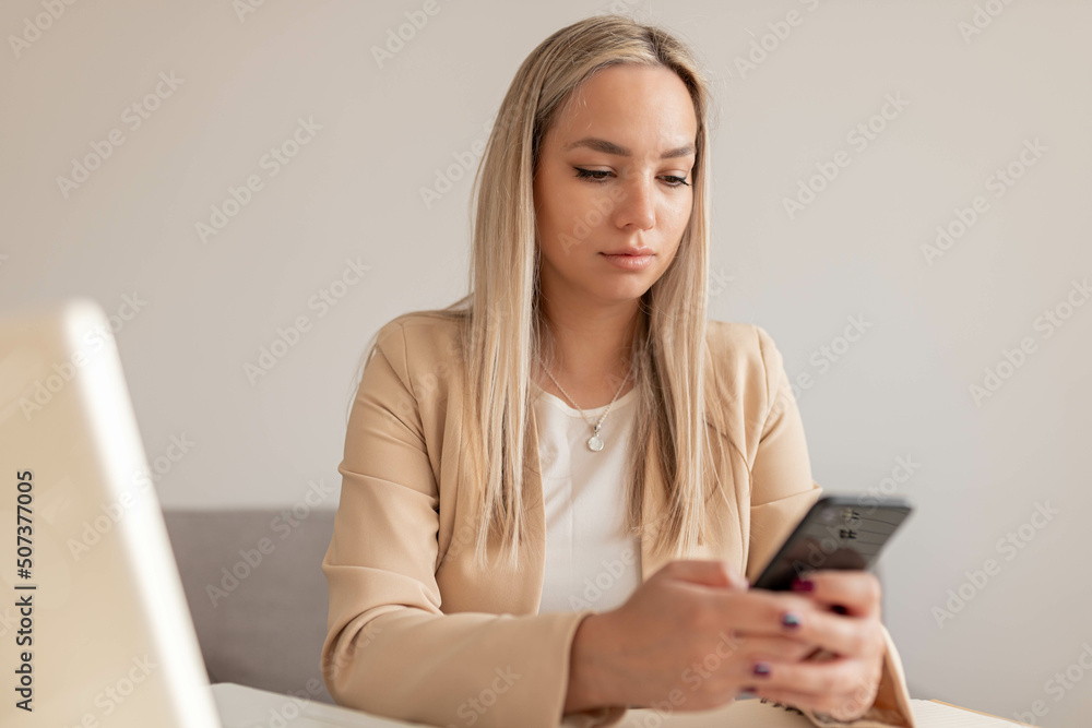 Happy charming woman using smartphone while working with laptop at home Happy charming woman using smartphone while working with laptop at home