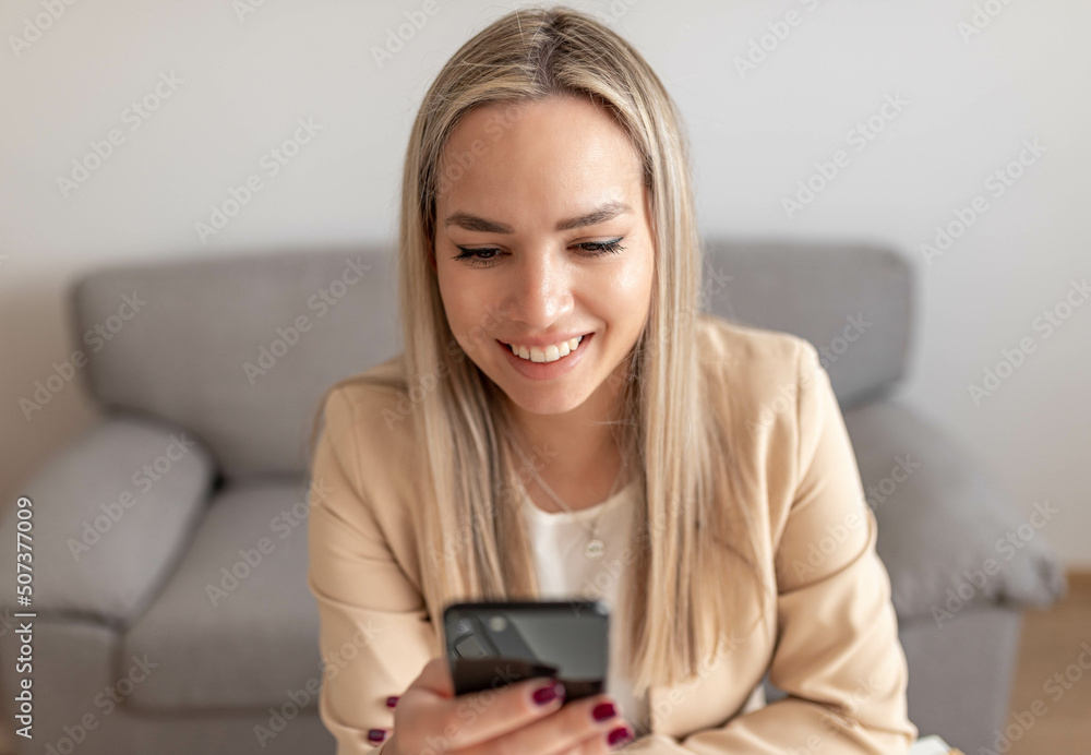 Happy charming woman using smartphone while working with laptop at home Happy charming woman using smartphone while working with laptop at home