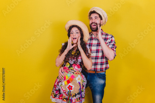 Beautiful couple dressed in typical clothes for a Festa Junina. Arraia de Sao Joao. Calling and screaming loudly, promotion. photo