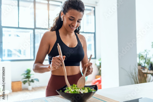 Beautiful young woman cooking while singing and listening music with headphones in the kitchen at home. photo