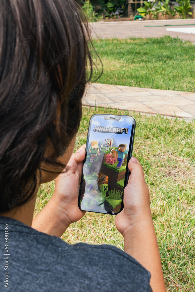 Naklejka premium Child sitting on grass with Minecraft mobile game app on smartphone screen. Rio de Janeiro, RJ, Brazil. May 2022