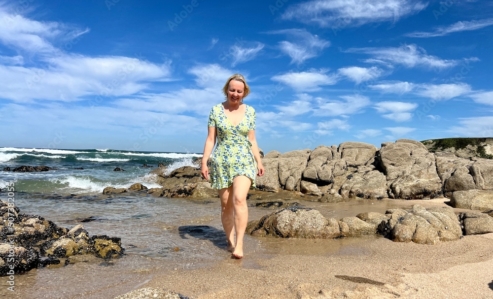 adult woman in a short dress on the sea an adult woman with a feminine figure stands against the backdrop of the sea, she has blond hair and an hourglass figure, she walks along the beach