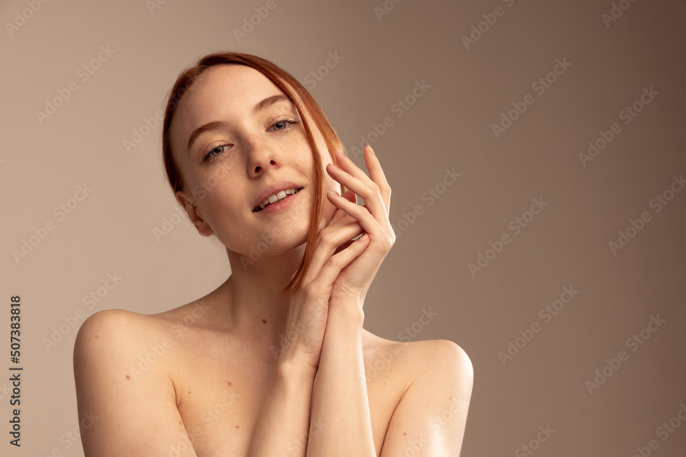 Portrait of young beautiful red-haired girl isolated over grey studio background. Skin care routine