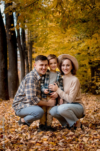 Portrait of happy young family on the background of autumn park. Mom, dad and son are smiling. Family autumn photo shoot