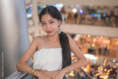A beautiful petite asian woman hanging out inside a mall by the ledge of the atrium. A pretty Filipina lady in a white crop top. photo
