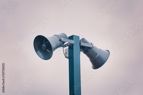 Hazard warning system. Tall metal column with two gray loudspeakers against cloudy sky. Providing security in the city, notification of emergencies. Copy space for text.