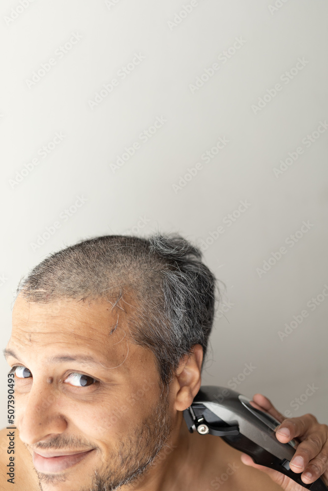Obraz premium Handsome gray-haired man is cutting hair himself.