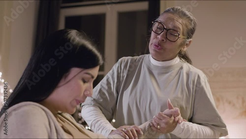 Woman having contractions at home and talking with midwife. Asian doula holding expecting mother hand, stroking her and comforting woman. Motherhood, pregnancy, childbirth concept