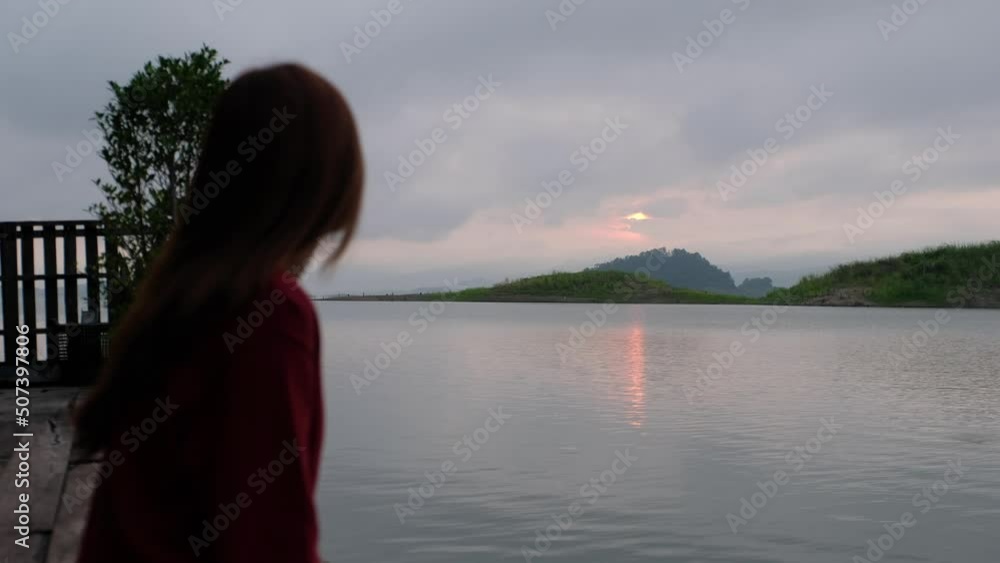 A young woman watching sunrise while sitting and relaxing by the water in a reservoir A young woman watching sunrise while sitting and relaxing by the water in a reservoir