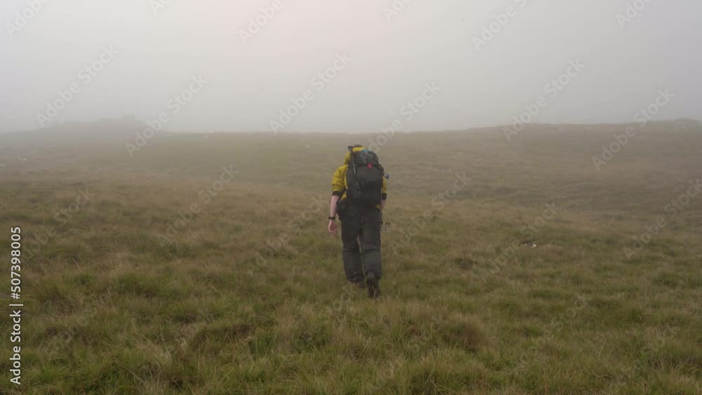 Man in Yellow Jacket Hiking up a grassy hill into the Misty Man in Yellow Jacket Hiking up a grassy hill into the Misty