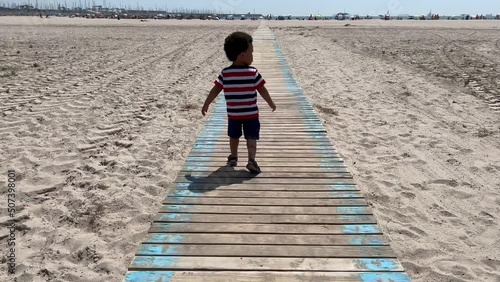 Two year old african child walkig on a  wooden gateway in a white sand beach in Valencia, Spain photo