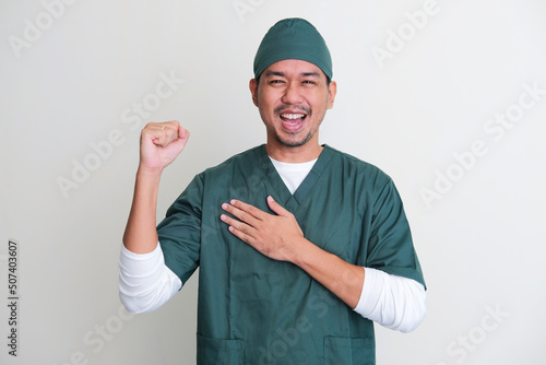 Asian hospital nurse clenched fist while one hand touching his chest showing excitement photo