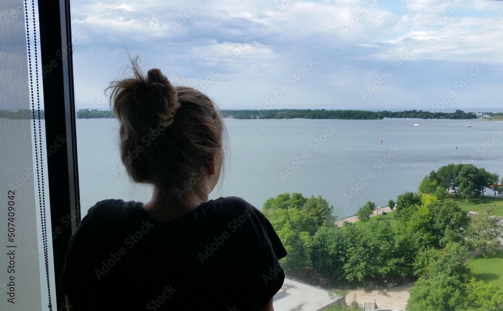 Fototapeta premium Woman looking out window over Lake Ontario in Toronto, Canada