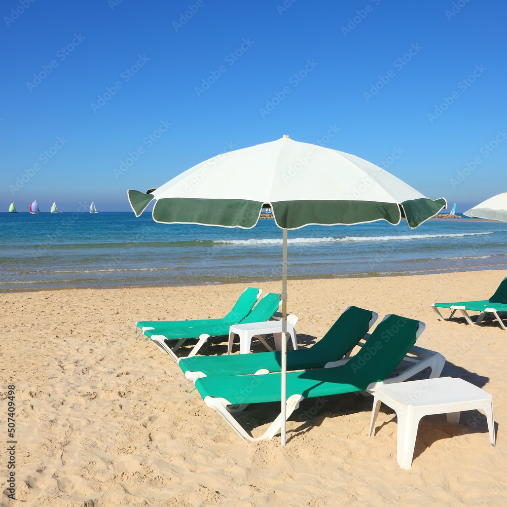 Sandy beach with sun umbrella and green lounges