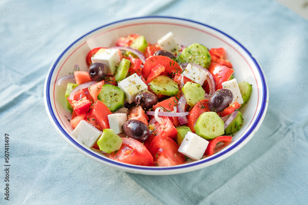 Greek salad with feta cheese, olives, tomato, cucumber and red onion, healthy vegeterian mediterranean diet food, low calories eating. Blue fabric background, top view Greek salad with feta cheese, olives, tomato, cucumber and red onion, healthy vegeterian mediterranean diet food, low calories eating. Blue fabric background, top view