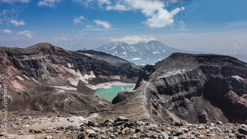 Amazing acid turquoise lake on top of an active volcano. The layered structure of the steep slopes of the crater, rocky soil is visible. The mountain against the blue sky. Kamchatka. Gorely Volcano photo