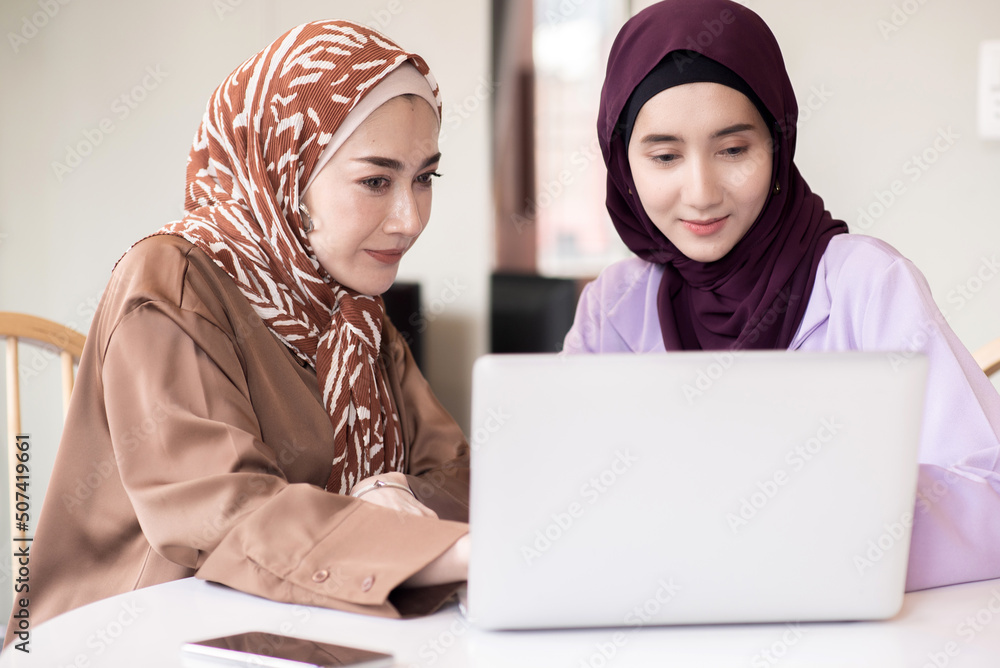 Two Muslim women using laptop for explaining business information in the room Two Muslim women using laptop for explaining business information in the room