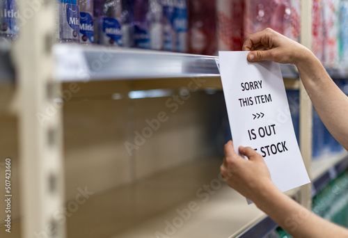 Shop assistant hanging a notice in empty shelves in a grocery store photo