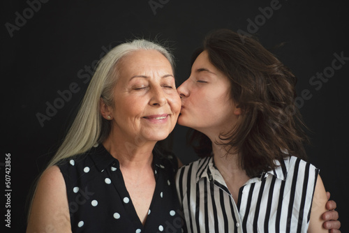 Portrait of senior grandmother with her granddaughter kissing her over black blackground