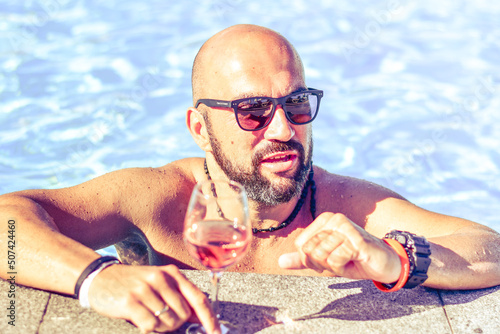 Portrait of a  happy smiling bearded Man beautiful  holding   a Glass of rose Wine by the swimming pool on the empty deck of a cruise liner.Vacation and travel conceptl photo