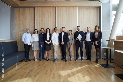 Group portrait of happy multiracial business people. Diverse team of smiling young and mature entrepreneurs or corporate employees standing together in modern office interior