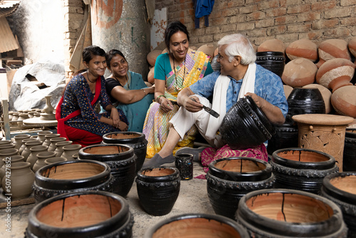 Happy Indian family of potters painting clay pots at workshop