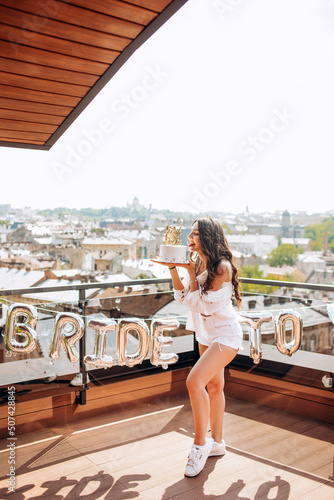 Beautiful girl in a white shirt and shorts posing with a cake on the roof of the house.