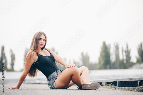 A female student sits cross-legged on the road in summer and looks at the camera natural background