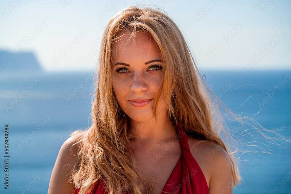 Smiling young woman in a red dress looks at the camera. A beautiful tanned girl enjoys her summer holidays at the sea. Portrait of a stylish carefree woman laughing at the ocean. Smiling young woman in a red dress looks at the camera. A beautiful tanned girl enjoys her summer holidays at the sea. Portrait of a stylish carefree woman laughing at the ocean.