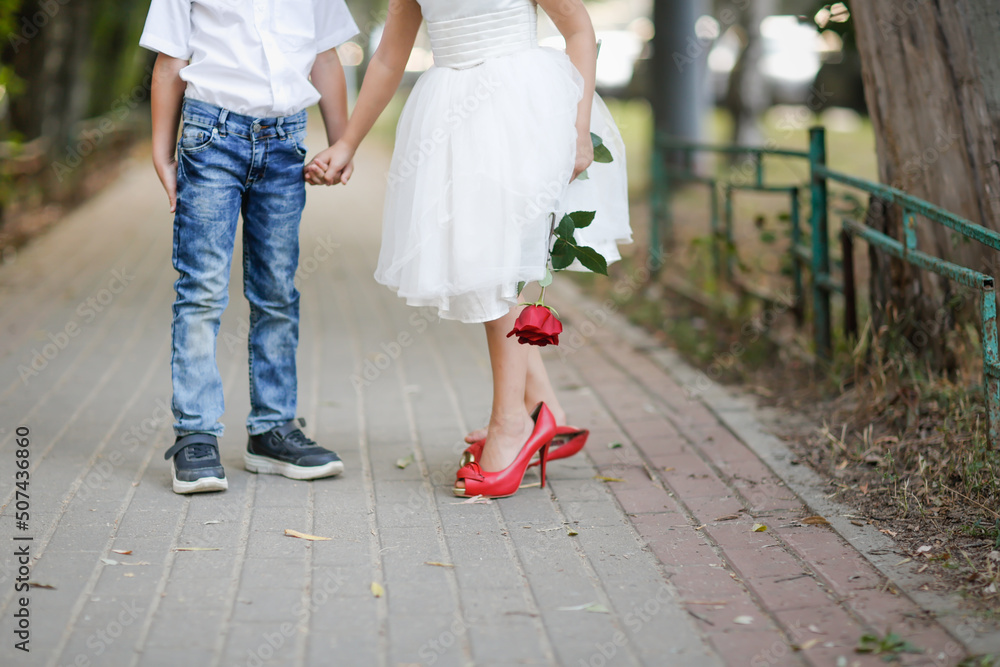 Obraz premium cute couple of children boy and girl with rose on walk in summer. Girl child in high heels, children play dating and courtship, relationship and growing up concept