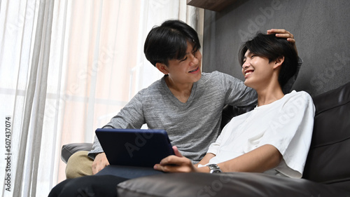 Loving young gay couple using digital tablet together in living room. Concept of sexual freedom and equal rights for LGBT community