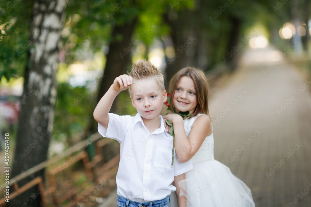 Cute couple children boy and girl hugs and holding rose on walk in summer, children play date and courtship, romantic and growing up concept
