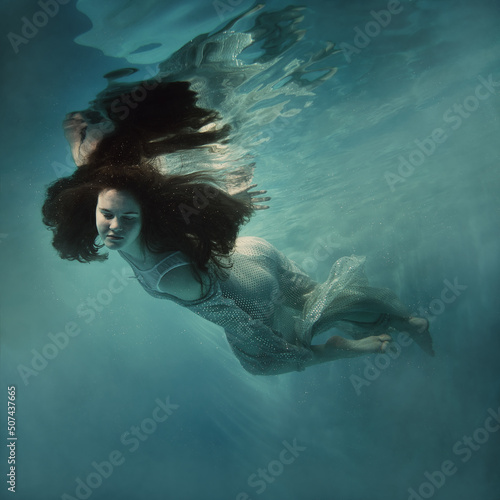 A girl in a shiny dress swims underwater © Dmitry