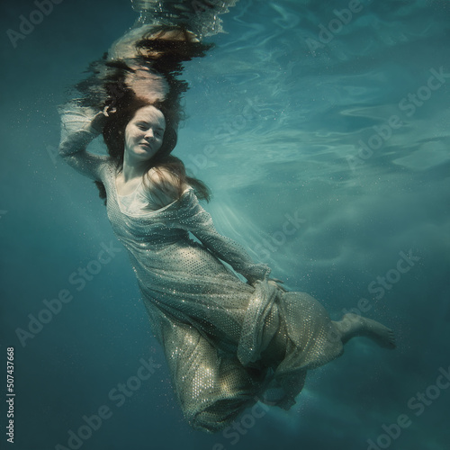 A girl in a shiny dress swims underwater