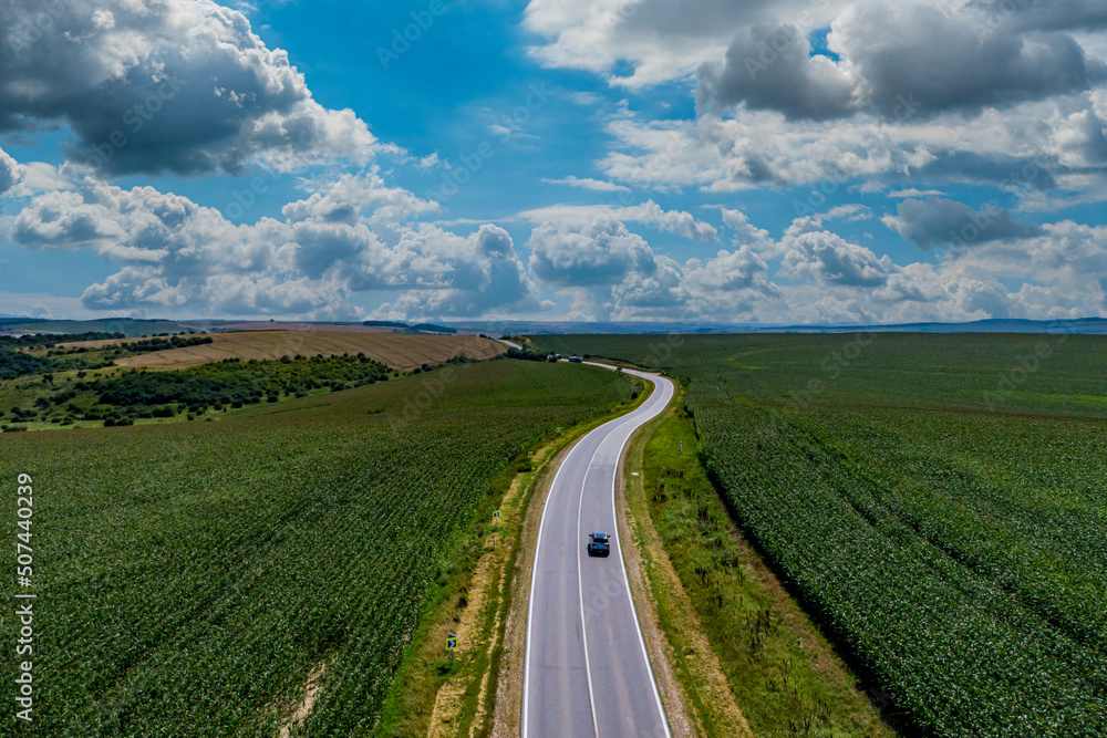 car driving on asphalt road along the green fields. beautiful clouds in the sky. Aerial view landscape. drone photography. transportation and travel concept.