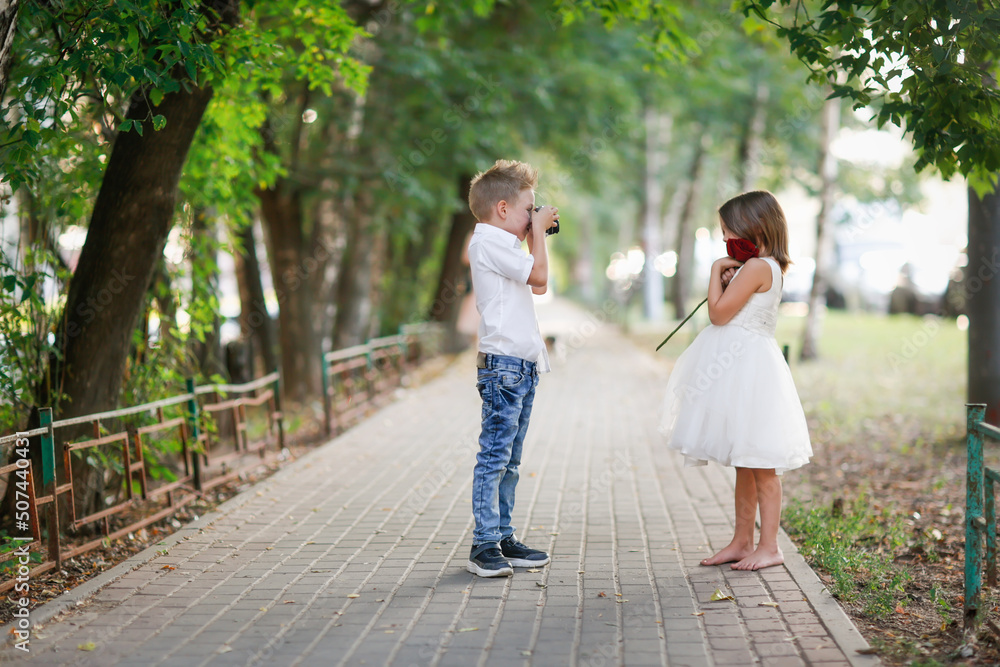 Funny romantic couple kids. boy with retro film camera photographs girl with rose, summer walks in park. Funny romantic couple kids. boy with retro film camera photographs girl with rose, summer walks in park.