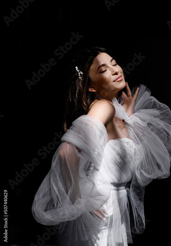 Beautiful young caucasian bride in white dress posing in the sun on a dark background. Close up