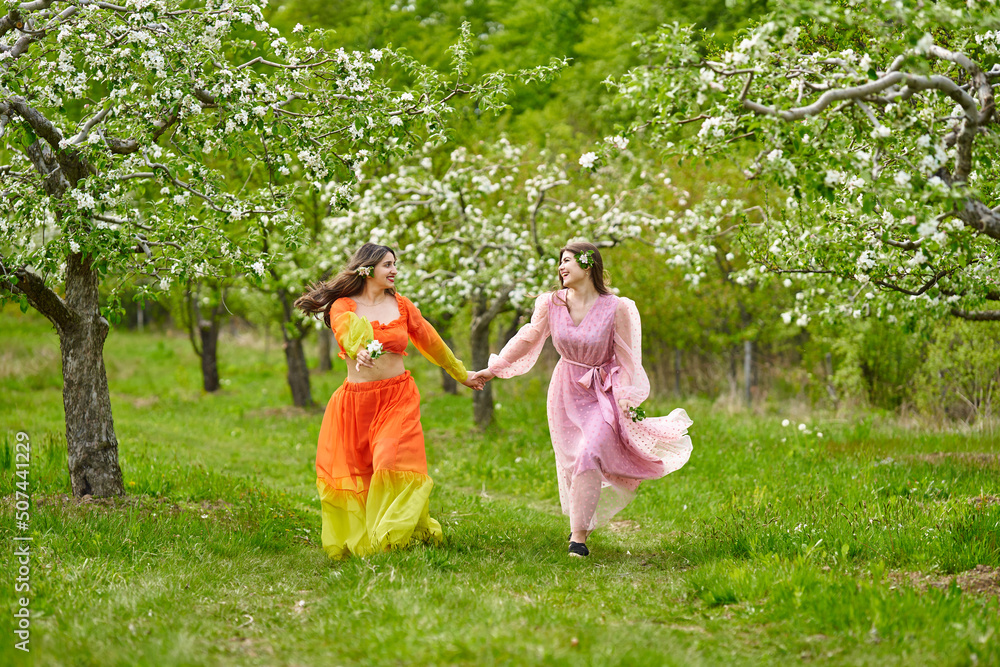 Two women of mixed race walking hand in hand through an orchard Two women of mixed race walking hand in hand through an orchard