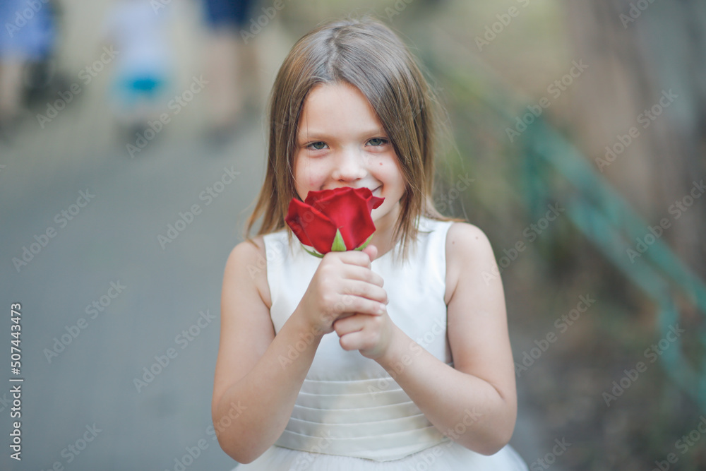 Cute european girl with rose, the child smells a big red rose Cute european girl with rose, the child smells a big red rose