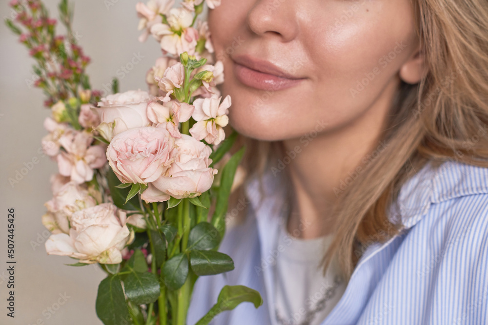 Horizontal close-up studio portrait of young woman holding beautiful pale pink flower bouquet near her face Horizontal close-up studio portrait of young woman holding beautiful pale pink flower bouquet near her face