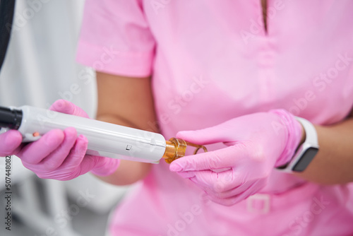 Doctor cosmetologist in protective gloves holds laser epilator in hands