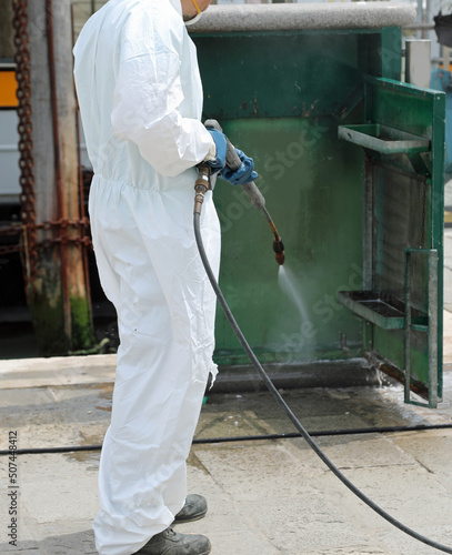 worker of the pest control company with protective suit while cleaning the street furniture with a powerful jet of water with a pressure washer to counteract the virus