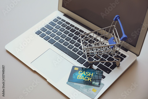 Modern laptop with small cart and cashback credit cards on light table