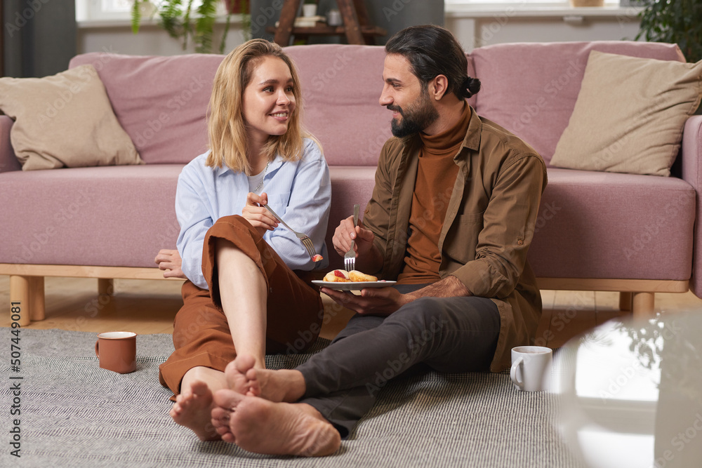 Handsome young man and attractive woman spending morning together sitting on floor in living room having breakfast Handsome young man and attractive woman spending morning together sitting on floor in living room having breakfast