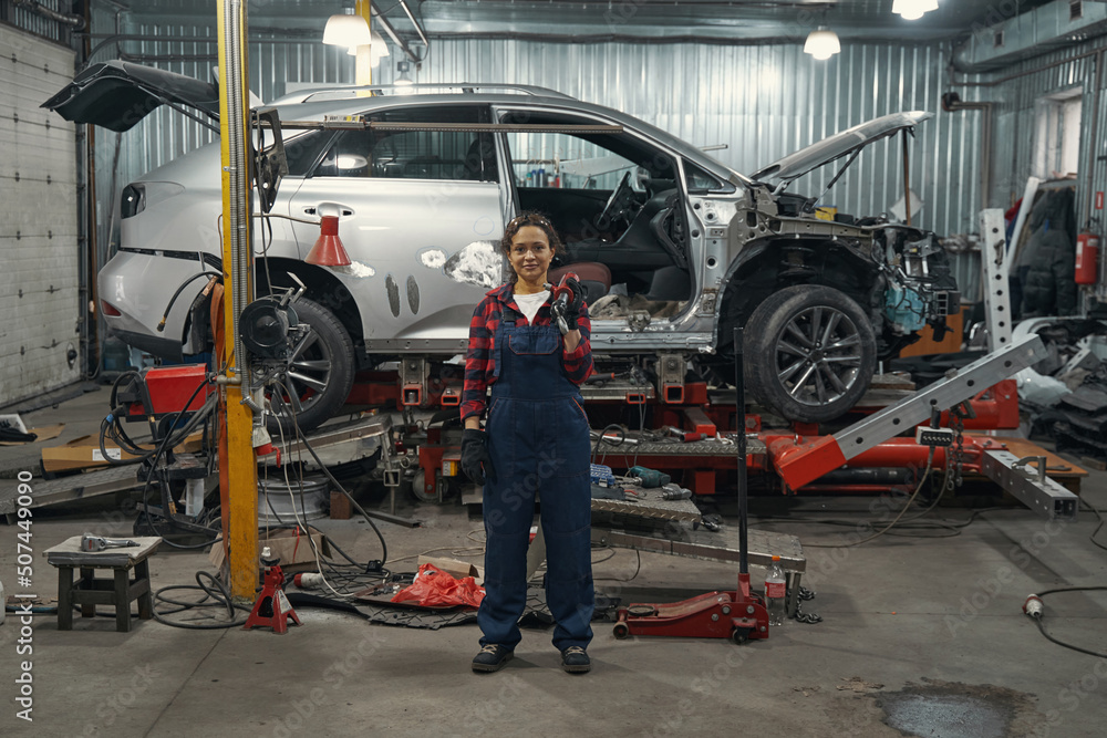 Fototapeta premium Woman auto mechanic standing near vehicle in car garage